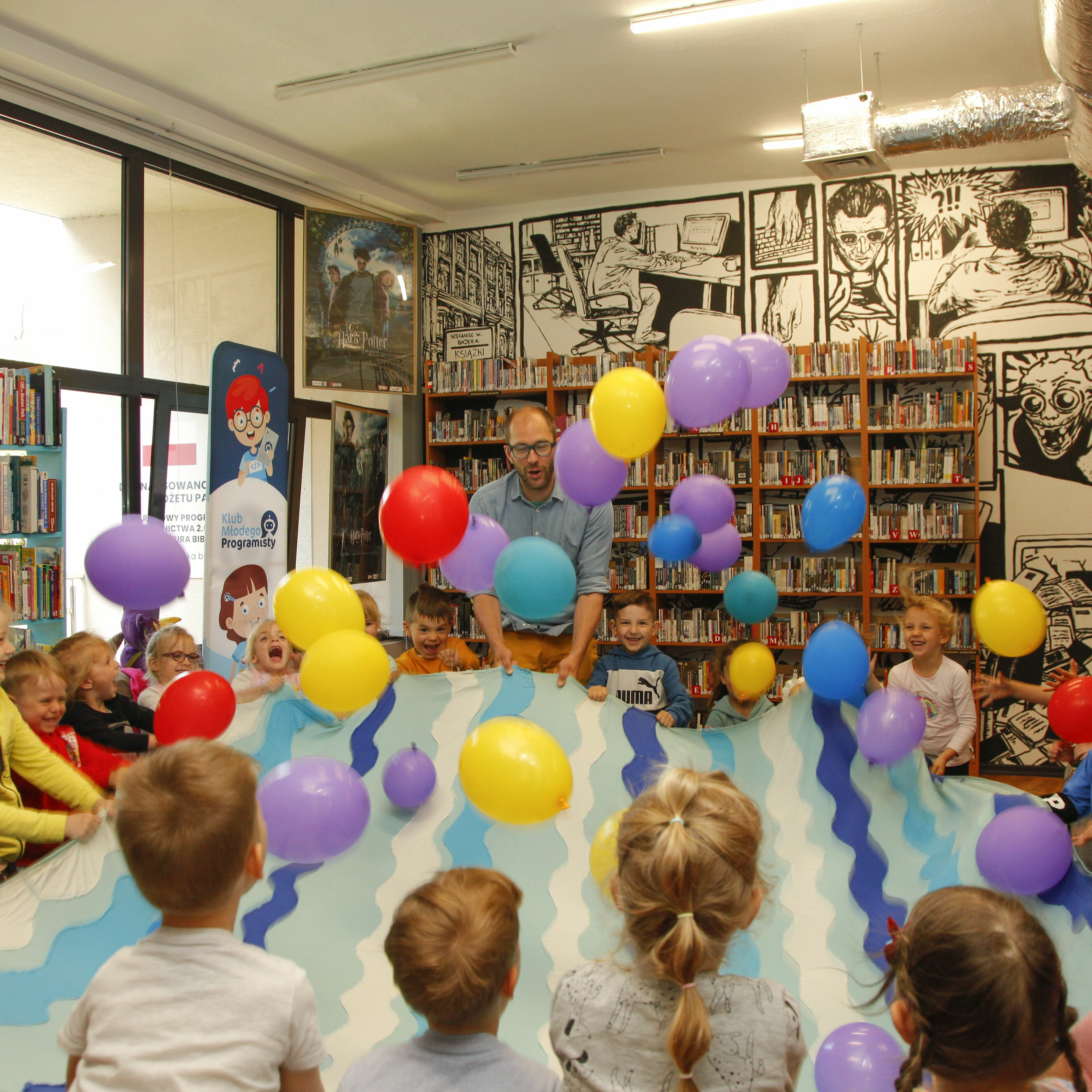 Pan Poeta z dziećmi trzymają materiał i podrzucają nim balony
