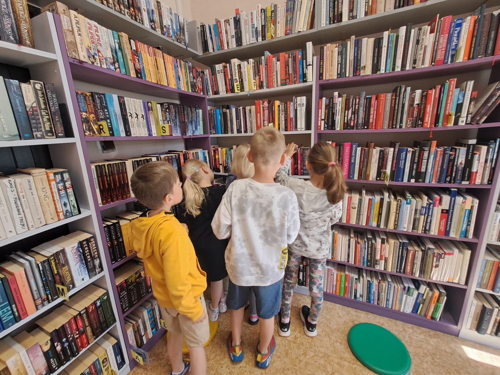 na zdjęciu regały z książkami i dzieci szukające na półkach książek